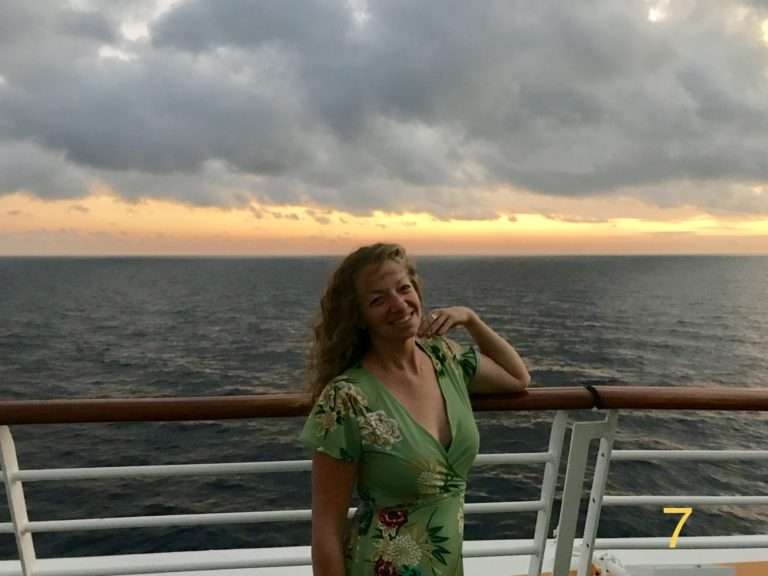 Suzannah Bianco in a green dress on a cruise ship with a sunset in the back ground