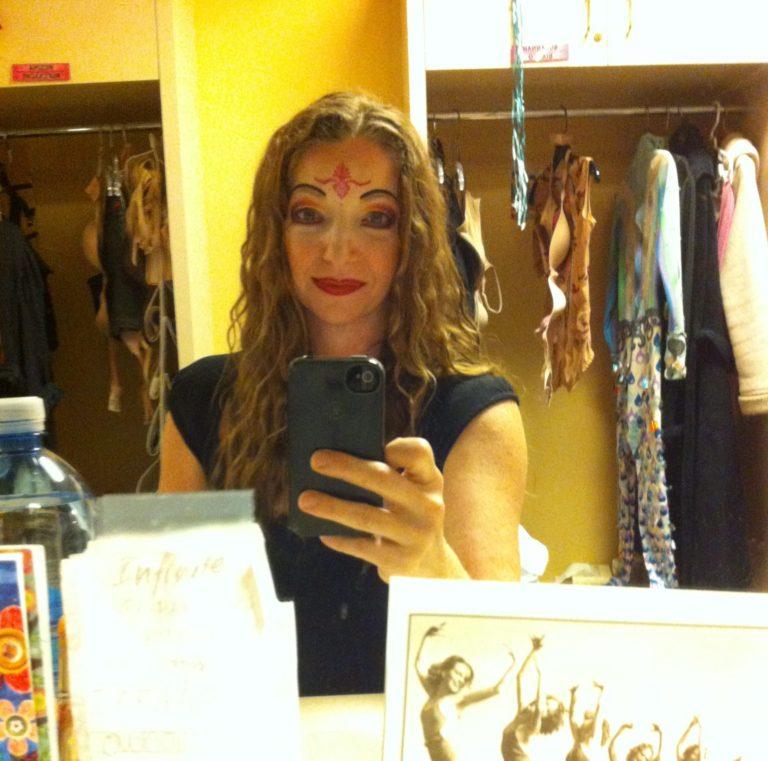 Suzannah Bianco in the dressing room at "O" by cirque Du Soleil in show make up taking a picture in the mirror and there are show costumes in the background.