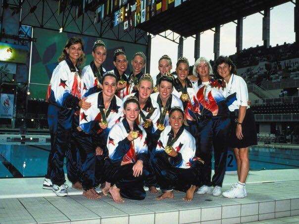 A photo showing the Synchronized artistic swimming 1996 Olympic Gold and the coaches Medalists displaying their medalss to the crowd after the awards ceremony. Suzannah Bianco is part of this team