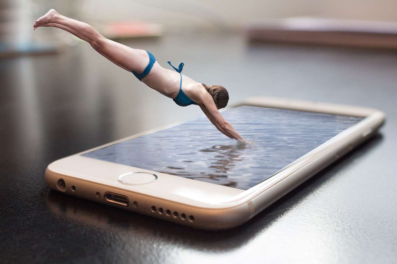 image of a call phone lying on a table and a CGI of a women in a blu bikini diving into water that is the screen of the cellular phone